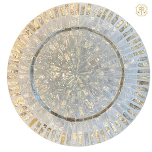 May include: Circular decorative plate with a mosaic design. The plate has a central circular pattern with radiating lines, surrounded by a border of rectangular tiles. The mosaic is mainly white and gold, creating a shimmering effect.