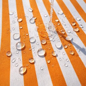 May include: Close-up of a striped orange and white fabric with water droplets. The fabric has vertical stripes and is textured. Water is being poured onto the fabric, creating droplets of various sizes.