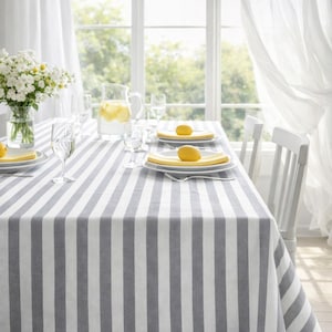 Könnte beinhalten: Ein Esstisch, gedeckt mit einer grau-weiß gestreiften Tischdecke. Der Tisch ist mit weißen Tellern, gelben Servietten und Zitronen gedeckt. Eine Glaskaraffe mit Limonade und eine Vase mit weißen Blumen sind ebenfalls vorhanden.