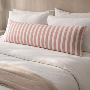 May include: A long, rectangular pillow with vertical stripes in soft pink and white, placed on a bed with white bedding. The pillow is approximately 40 inches long. The bed has a neutral-toned headboard and a beige throw.