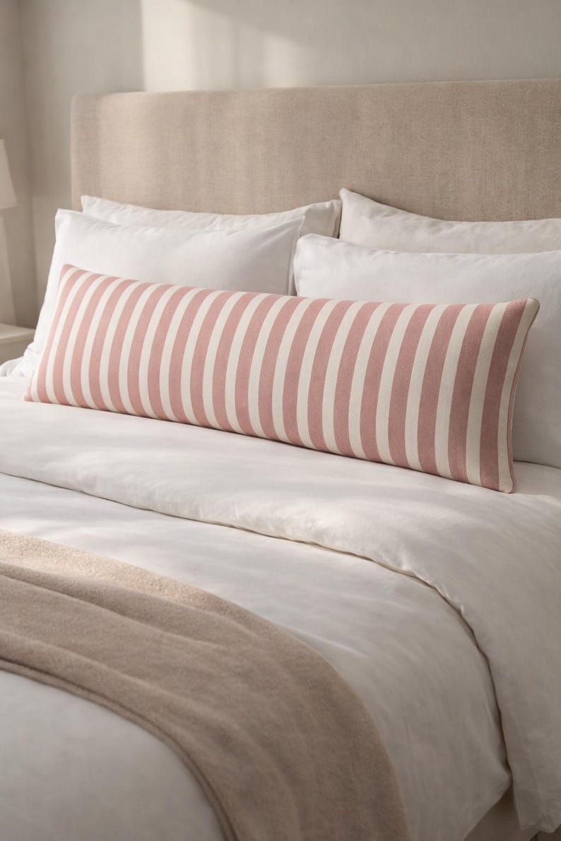 May include: A long, rectangular pillow with vertical stripes in soft pink and white, placed on a bed with white bedding. The pillow is approximately 40 inches long. The bed has a neutral-toned headboard and a beige throw.
