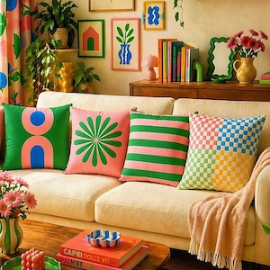 May include: A living room scene with a cream-colored sofa adorned with decorative throw pillows in green, pink, and checkered patterns. Artwork with floral and geometric designs hangs on the wall. A wooden coffee table displays books and a decorative tray.