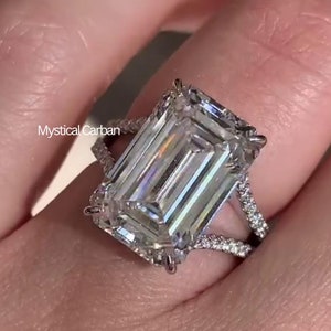 May include: A silver ring featuring a large, clear emerald-cut diamond set in a pave setting. The ring has a split shank with a delicate diamond band.