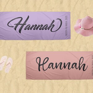 Puede incluir: Dos toallas de playa personalizadas, una lavanda y otra rosa, cada una con el nombre "Hannah" en escritura negra. Tambi&eacute;n se muestra un sombrero para el sol rosa con detalles florales y un par de chanclas blancas.