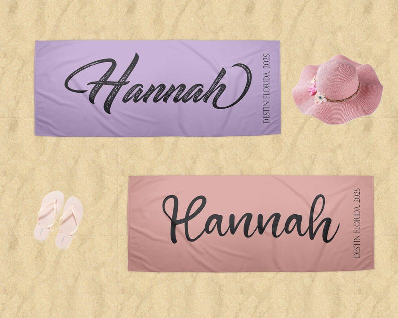 Puede incluir: Dos toallas de playa personalizadas, una lavanda y otra rosa, cada una con el nombre "Hannah" en escritura negra. Tambi&eacute;n se muestra un sombrero para el sol rosa con detalles florales y un par de chanclas blancas.