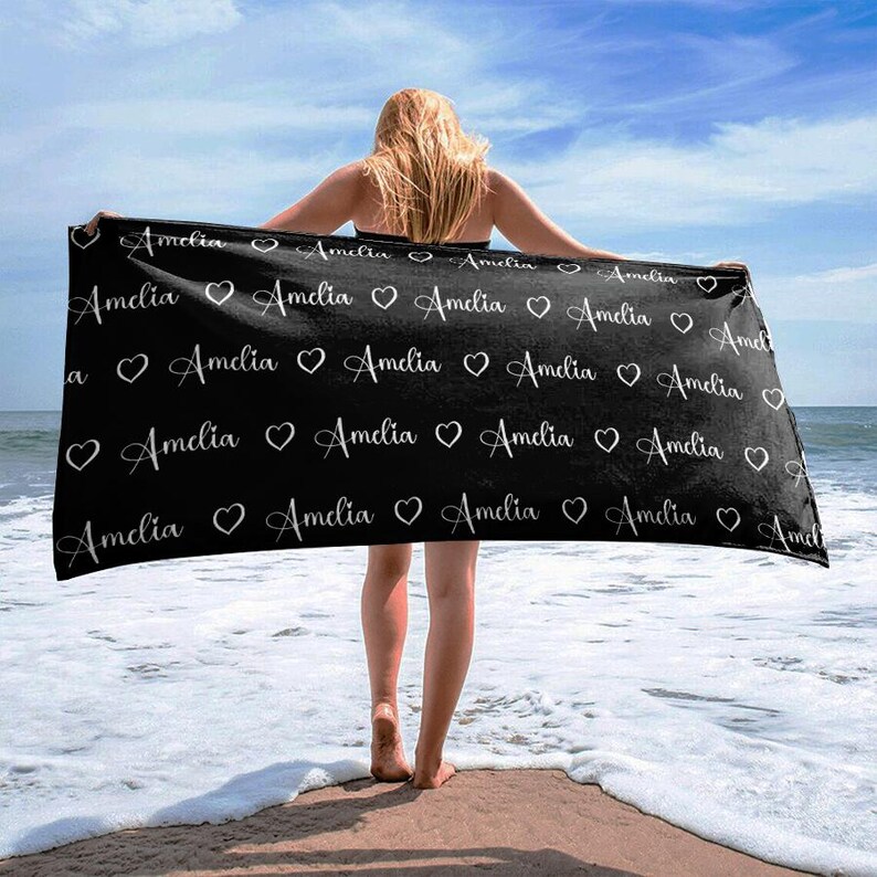 May include: Black beach towel with the name "Amelia" repeated in white cursive lettering with a heart between each name.