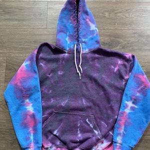 May include: A tie-dye hoodie with a purple, pink, and blue color scheme. The hoodie has a drawstring hood and a kangaroo pocket.