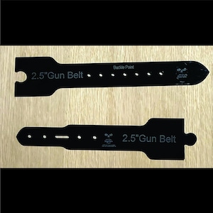 May include: Two black 2.5-inch gun belts are displayed on a light wood surface. The belts have a rectangular shape with rounded edges and several holes. The text "2.5" Gun Belt" and "Buckle Point" are visible.