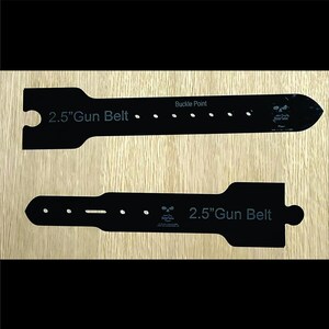 May include: Two black 2.5-inch gun belt templates with the text "2.5" Gun Belt" and "Buckle Point". The templates have a series of holes and a skull logo. The templates are on a light wood grain surface.