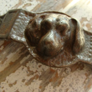 May include: A cast iron door handle with a dog's head design. The handle is rusty and has a dark brown color.
