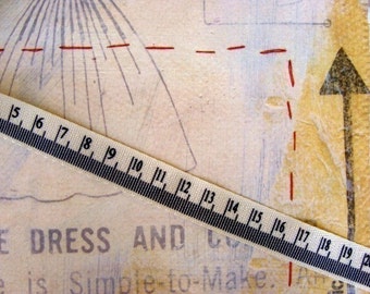 May include: A close-up of a white fabric measuring tape with black markings. The tape is laid diagonally across a piece of paper with a red dashed line and the text "CE DRESS AND" printed on it.