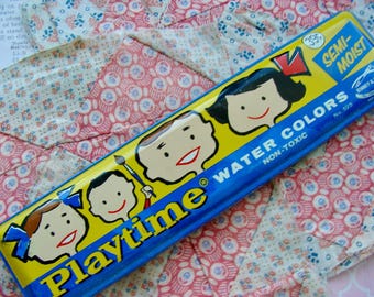 May include: A blue and yellow metal tin with the words "Playtime Water Colors" and "Semi-Moist" printed on it. The tin features four cartoon children with paintbrushes and is labeled "Non-Toxic".