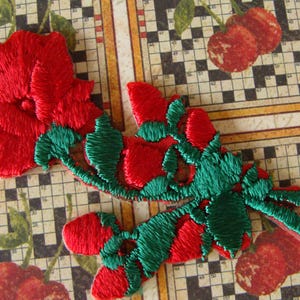 May include: Embroidered red flower and leaf patches with green accents. The patches are on a background with a crossword puzzle design and cherry illustrations. These patches can be used for clothing or craft projects.