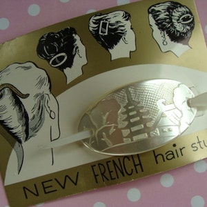 Puede incluir: Una pinza para el pelo ovalada plateada con un diseño decorativo y un peine de plástico blanco. El embalaje tiene el texto "NEW FRENCH hair style".