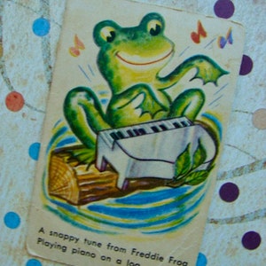 May include: A green frog playing a white piano on a brown log. The text reads "A snappy tune from Freddie Frog Playing piano on a log."