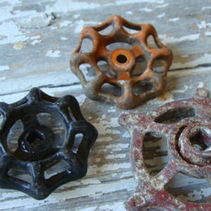 May include: Three vintage metal water valve handles. One is black, one is orange, and one is red with rust. The handles are all in the shape of a star with six points.