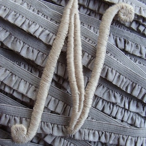 May include: A close-up of a gray fabric with a white fabric letter N sewn on top. The fabric has a ruffled edge.