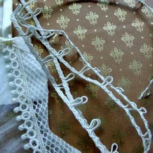 May include: White lace trim with loops, perfect for adding a touch of elegance to any project. The trim is shown on a brown background with a repeating pattern.