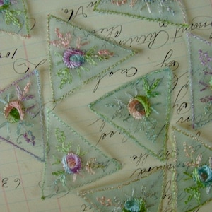 May include: Assortment of delicate, triangular, sheer fabric pieces with embroidered floral designs in shades of pink, blue, and green. The fabric is translucent and has a vintage aesthetic.