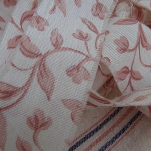 Peut inclure: Gros plan sur un tissu blanc avec un motif floral rose. Le tissu est pli&eacute; et pr&eacute;sente un bord effiloch&eacute;.