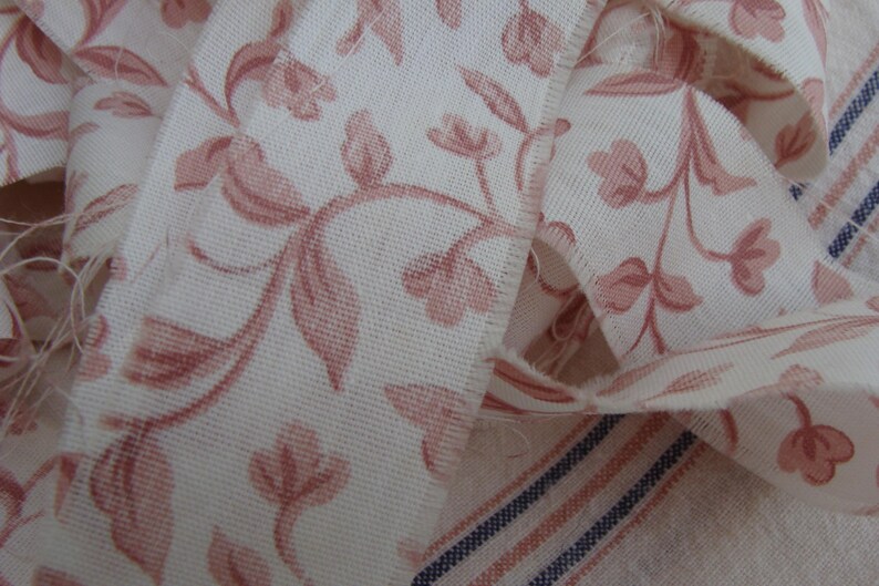 Peut inclure: Gros plan sur un tissu blanc avec un motif floral rose. Le tissu est pli&eacute; et pr&eacute;sente un bord effiloch&eacute;.