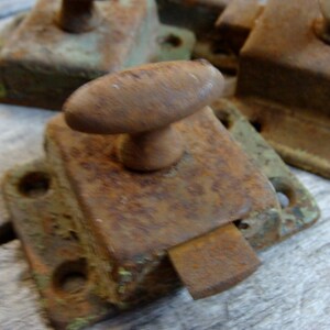 May include: A set of four antique rusty metal door latches with a green patina. The latches have a simple design with a rounded knob and a rectangular plate.