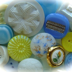 May include: Assortment of colorful buttons in various shapes and sizes, including blue, yellow, white, and a floral design. The buttons are made of plastic and have a shiny finish.