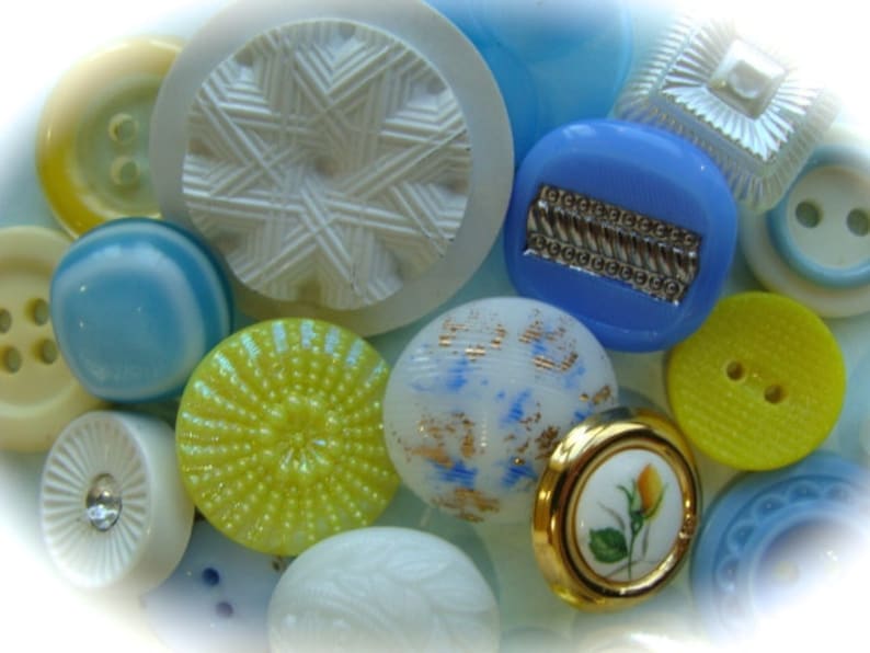 May include: Assortment of colorful buttons in various shapes and sizes, including blue, yellow, white, and a floral design. The buttons are made of plastic and have a shiny finish.