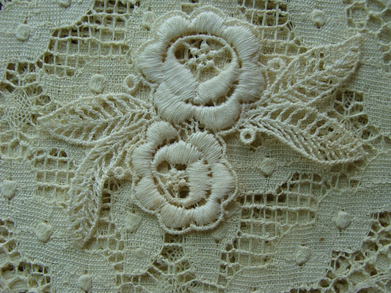 May include: Close-up of delicate white lace fabric with a floral design. The lace features two embroidered flowers with intricate details and leaves.
