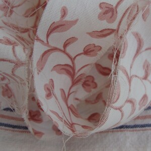 Peut inclure: Gros plan sur un tissu blanc &agrave; motif floral rose. Le tissu est pli&eacute; sur lui-m&ecirc;me, montrant le bord brut du mat&eacute;riau.