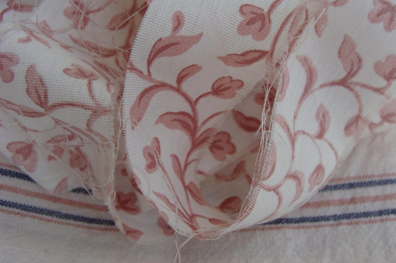 Peut inclure: Gros plan sur un tissu blanc &agrave; motif floral rose. Le tissu est pli&eacute; sur lui-m&ecirc;me, montrant le bord brut du mat&eacute;riau.