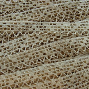 May include: A close-up of a pile of beige crocheted lace trim. The lace has a delicate, intricate pattern with small holes throughout.