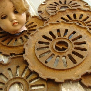 May include: A collection of rusty metal planter discs with a decorative, circular design. The discs have a raised edge and a central hole. The discs are arranged in a pile, with some overlapping.