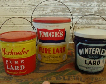 May include: Three vintage metal lard containers with red, yellow and blue labels. The containers are labelled "Emge's Pure Lard", "Marhoefer Pure Lard", and "Winterlein Lard".