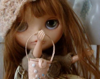 May include: A doll with long brown hair wearing a crocheted hat with a white flower, a brown and white dress, and holding a small white and blue beaded purse.