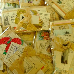 May include: A collection of vintage ephemera, including postcards, envelopes, and paper scraps, tied together with a yellow ribbon. The ephemera features various designs, including flowers, text, and illustrations.