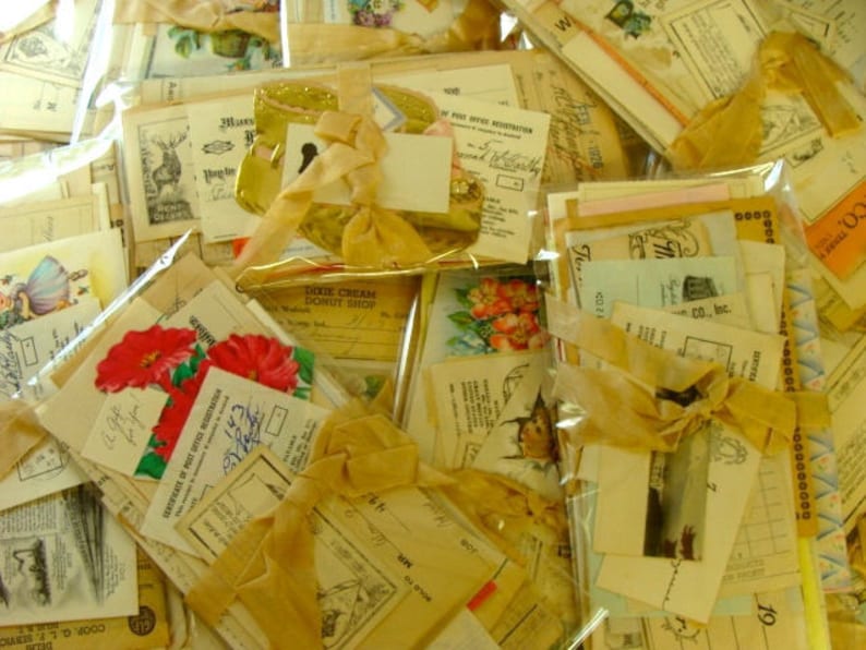 May include: A collection of vintage ephemera, including postcards, envelopes, and paper scraps, tied together with a yellow ribbon. The ephemera features various designs, including flowers, text, and illustrations.