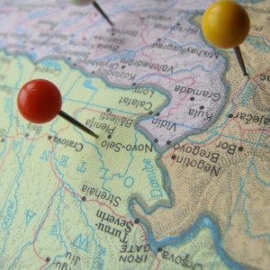May include: A map of Europe with three push pins, one red, one white, and one yellow, marking locations on the map.