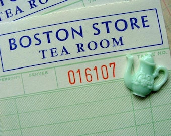 Może przedstawiać: Winietkowy paragon z Boston Store Tea Room z zielonym plastikowym breloczkiem w kształcie czajnika. Paragon ma numer stolika 016107.