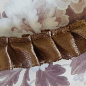 May include: Brown satin ribbon trim with a pleated design. The trim is folded and has a soft, luxurious look.