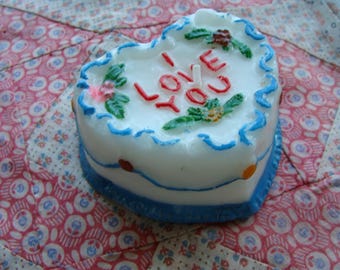 May include: A white heart-shaped cake with blue and white frosting. The cake is decorated with red and green icing and says "I Love You".