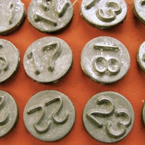 May include: Close-up of twelve silver metal number stamps, each with a different number from 1 to 12. The stamps are arranged in a grid pattern on a red surface.