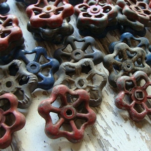 May include: A collection of vintage metal knobs with a starburst design. The knobs are in various shades of red, blue, and gray. Some of the knobs are stacked on top of each other.