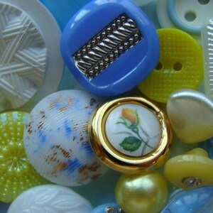 May include: Assortment of colorful buttons in various shapes and sizes, including round, square, and star-shaped buttons. Some buttons have a white background with blue and gold accents, while others have a yellow background with white accents. There are also buttons with a blue background and gold accents.