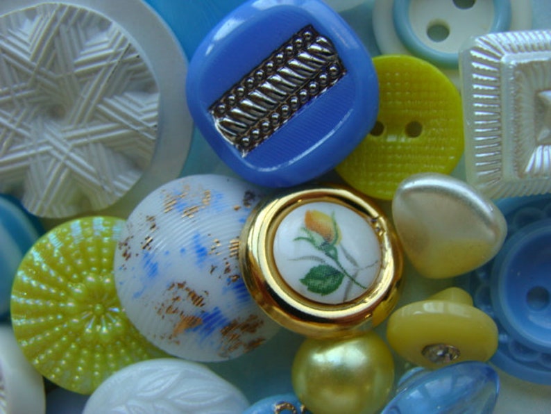May include: Assortment of colorful buttons in various shapes and sizes, including round, square, and star-shaped buttons. Some buttons have a white background with blue and gold accents, while others have a yellow background with white accents. There are also buttons with a blue background and gold accents.