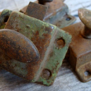 May include: Close-up of three rusty metal door latches. The latches are in various shades of green, brown, and black. The latches have a variety of shapes and sizes.