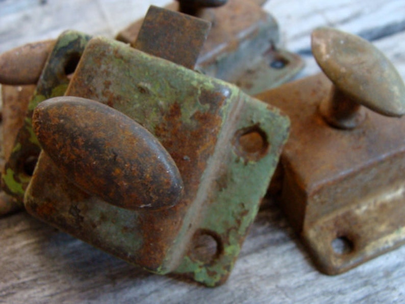 May include: Close-up of three rusty metal door latches. The latches are in various shades of green, brown, and black. The latches have a variety of shapes and sizes.