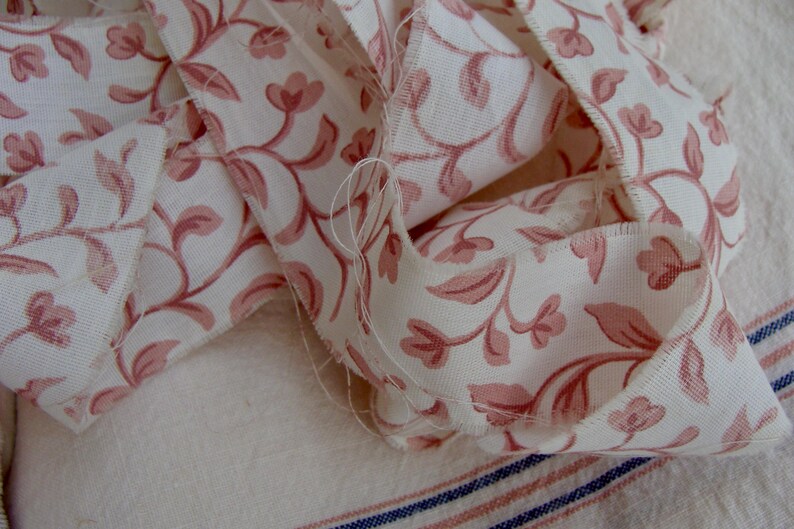 Peut inclure: Un gros plan sur un ruban en tissu floral rose et blanc. Le ruban est pli&eacute; et superpos&eacute;, montrant le motif floral complexe.