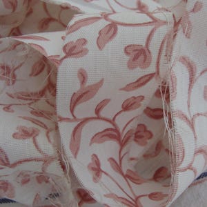 Peut inclure: Un gros plan sur un tissu blanc avec un motif floral rose. Le tissu est pli&eacute; et montre le d&eacute;tail du motif.