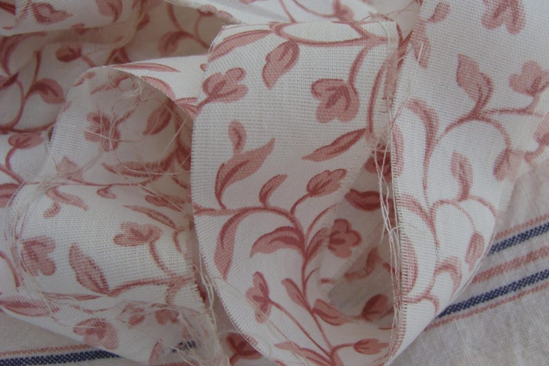 Peut inclure: Un gros plan sur un tissu blanc avec un motif floral rose. Le tissu est pli&eacute; et montre le d&eacute;tail du motif.